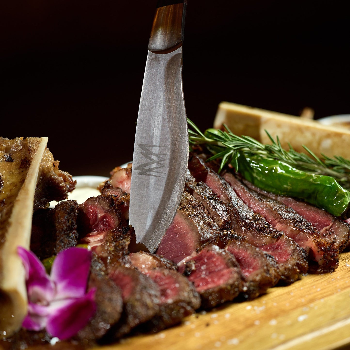 Steak on a wooden plate with a knife, garnished with herbs.