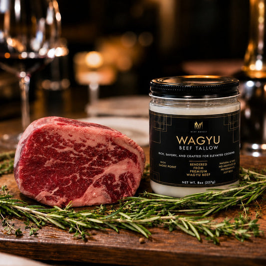 A jar of Wagyu beef tallow next to a raw marbled beef roast on a wooden cutting board with rosemary sprigs, set in a warm, blurred dining environment with wine glasses and tableware.